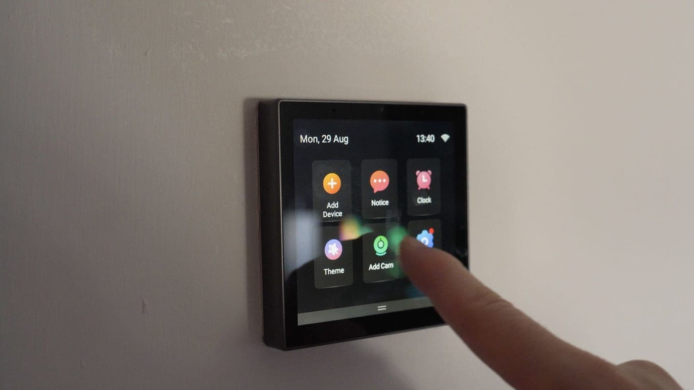 A wall-mounted NSPanel touchscreen being tapped